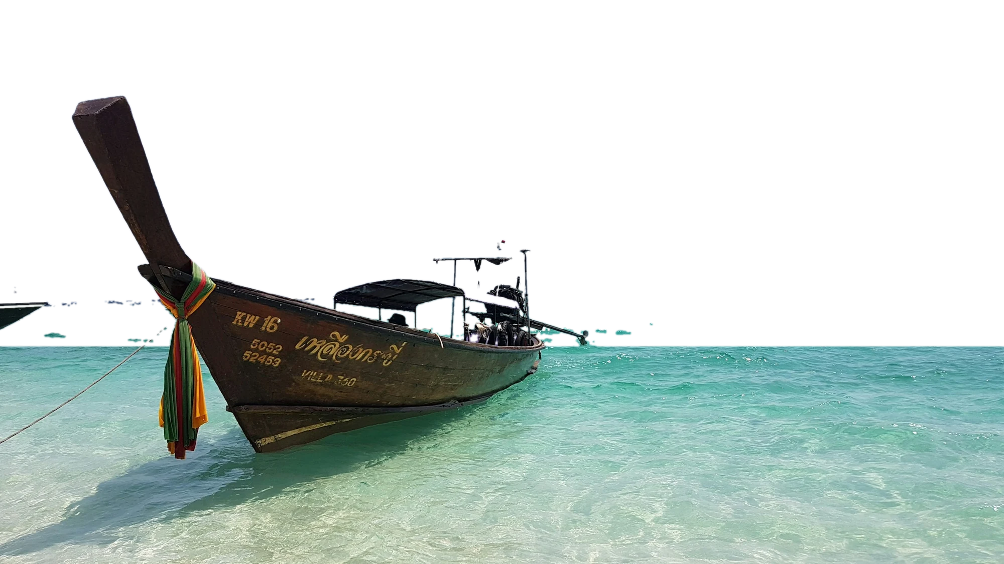 Wooden longtail boat with colourful ribbons on its tall bow, floating in clear turquoise water under a pale blue sky